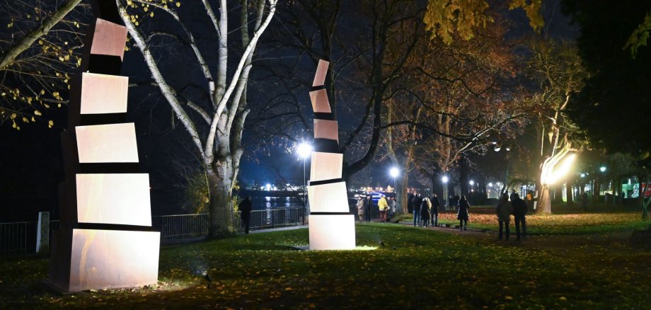 Die Ausstellung "outside RHEINside" umfasst großformatige Drucke, Bauminstallationen und eine Toninstallation, Großskulpturen sowie eine Landschaftsprojektion. Das Foto zeigt zwei beleuchtete Installationen in den Rheinanlagen.