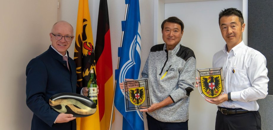 Empfang im Büro des Bopparder Bürgermeisters: Keiichi Hamanaka (Mitte) Bürgermeister von Ome, und Masayoshi Kusano (rechts), Abteilungsleiter für internationale Beziehungen bei der Stadt Ome, sind zu Gast in Boppard und überreichten Boppards Bürgermeister Jörg Haseneier (links) eine Flasche Wein aus in Ome gewachsenen Bopparder Reben und einen Teller aus Japan. 