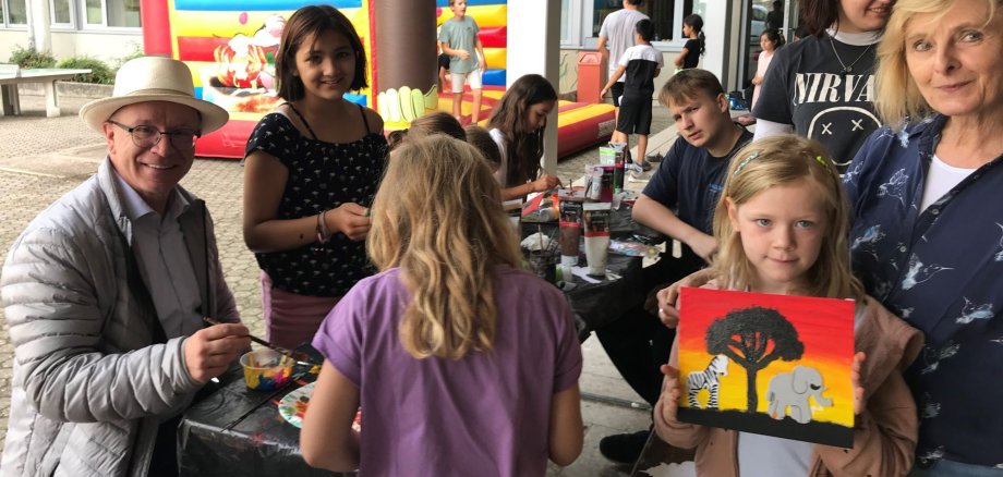 Boppards Bürgermeister Jörg Haseneier (links) beim Besuch der Sommerferienaktion. Die junge Amalia präsentiert ihr gemaltes Bild.  Die Leiterin der AWO Boppard, Stephanie Kolz, bewundert das gelungene Werk (rechts). 